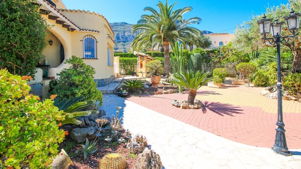 A courtyard with a paved walkway, palm trees, and a building with a blue window. - Villa with private pool in Denia (Denia)