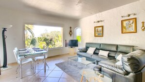 A living room with a glass dining table, a leather sofa, a TV, and a window with a view of greenery. - Villa with private pool in Denia (Denia)