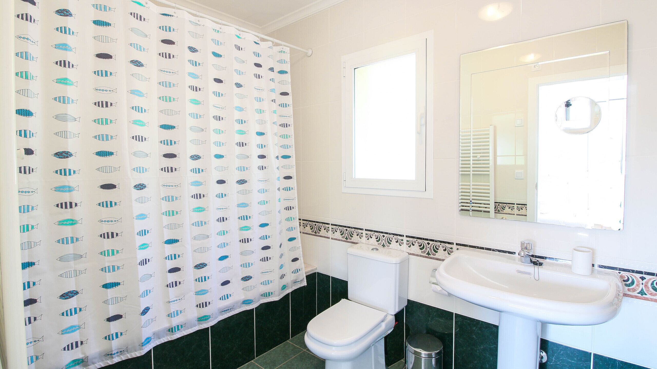 A bathroom with a toilet, sink, and a shower curtain with a fish pattern.