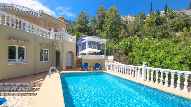 A swimming pool with blue water, surrounded by a white balustrade. There are lounge chairs and a covered area with a white umbrella. - Villa with panoramic views all inclusive in Denia (Denia)