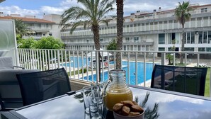 Une table avec un verre de jus d’orange, une bouteille et un bol de biscuits, donnant sur une piscine et un immeuble doté de balcons.