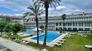 Un hĂŽtel dotĂ© dâune piscine, de palmiers et dâun espace salon abritĂ©.