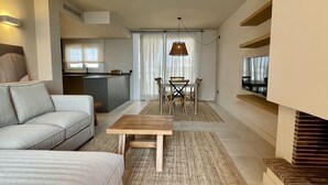 Un salon moderne comprenant un canapé, une table à manger avec des chaises, un coin cuisine et un téléviseur fixé au mur.