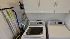 A laundry room with two washing machines, a drying machine, and a rack with cleaning tools.