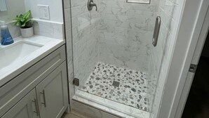 A modern bathroom with a glass-enclosed shower, marble tiles, a small plant, and a sink with a mirror.