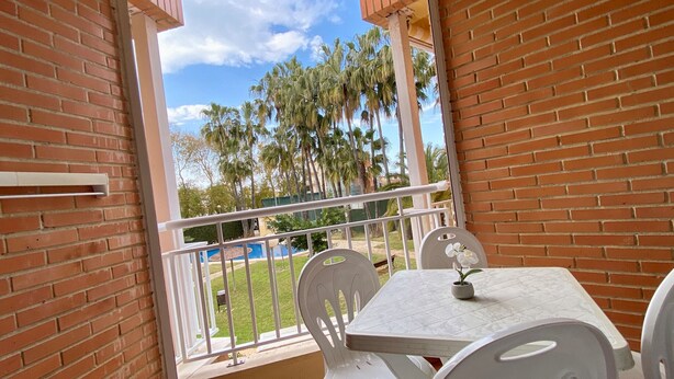 A balcony with a white table and chairs, a small potted plant, and a view of palm trees and a pool. - MED 19 with paddel court (Denia)