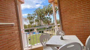 A balcony with a white table and chairs, a small potted plant, and a view of palm trees and a pool.