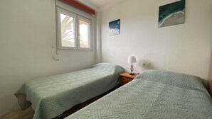 A room with two beds, a window, a nightstand with a lamp, and two wall-mounted paintings. - MED 19 with paddel court (Denia)