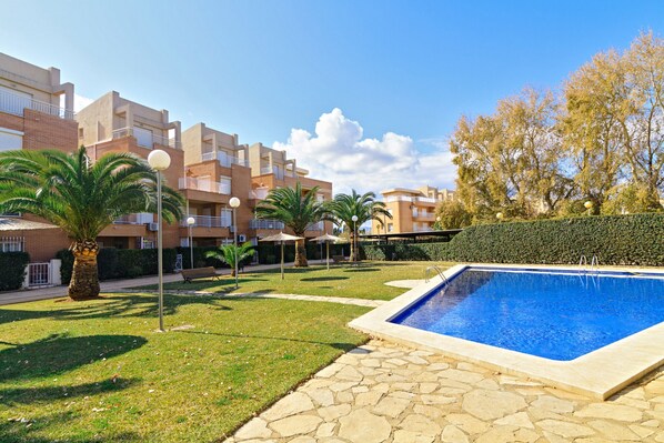 A swimming pool, palm trees, and a building with balconies.