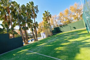 A tennis court with surrounding palm trees and a building in the background.