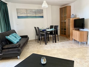A living room with a sofa, a dining table with chairs, a TV on a wooden cabinet, and a painting on the wall.