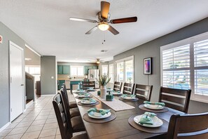 A dining area with a long table set for six, wooden chairs, a ceiling fan, and a view of the kitchen in the background. - Heated Pool.  3 King Rooms! Sleeps 9! (Glendale)