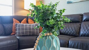 A living room with a teal vase with wooden beads on a wooden tray, a white table, and a dark leather couch with patterned cushions. - 4BR w pool, fire pit, 3 king rooms (Glendale)