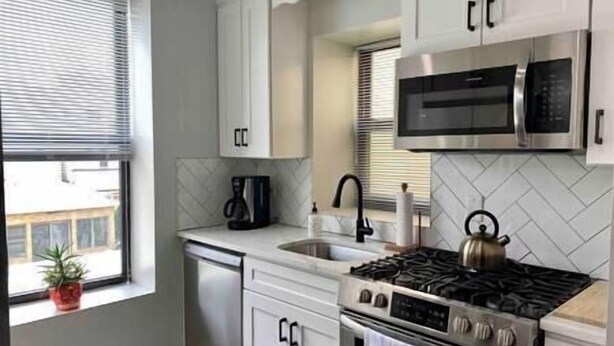 A kitchen with white cabinets, a stainless steel stove, a microwave, and a dishwasher. - The Monrow Suite! (West New York)