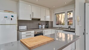 Une cuisine moderne avec des armoires blanches, un four encastré, un four à micro-ondes et un grand îlot central doté d’une planche à découper en bois.