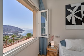 A bedroom with a large window, a bedside table with a lamp, a bed with pillows, and a wall-mounted artwork. - Holiday Home 'Casa Palmeras' with Sea Views, Wi-Fi and Air Conditioning (Almuñécar)
