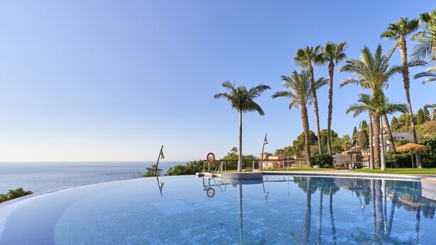 Une magnifique piscine à débordement d’un bleu profond, offrant une vue sur l’océan et les palmiers.