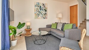 Un salon moderne avec un canapé d’angle, une table basse en verre, une plante en pot et un tableau accroché au mur.