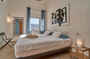 A bedroom with a bed, a bedside table with a lamp, a window with curtains, a wall-mounted mirror, and a painting. - Holiday Home 'Casa Palmeras' with Sea Views, Wi-Fi and Air Conditioning (Almuñécar)