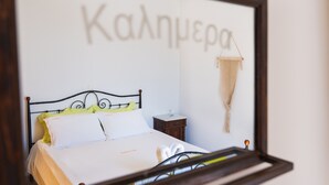 Een netjes opgemaakt bed met hoofdbord, een nachtkastje met lamp en een macramé wanddecoratie.