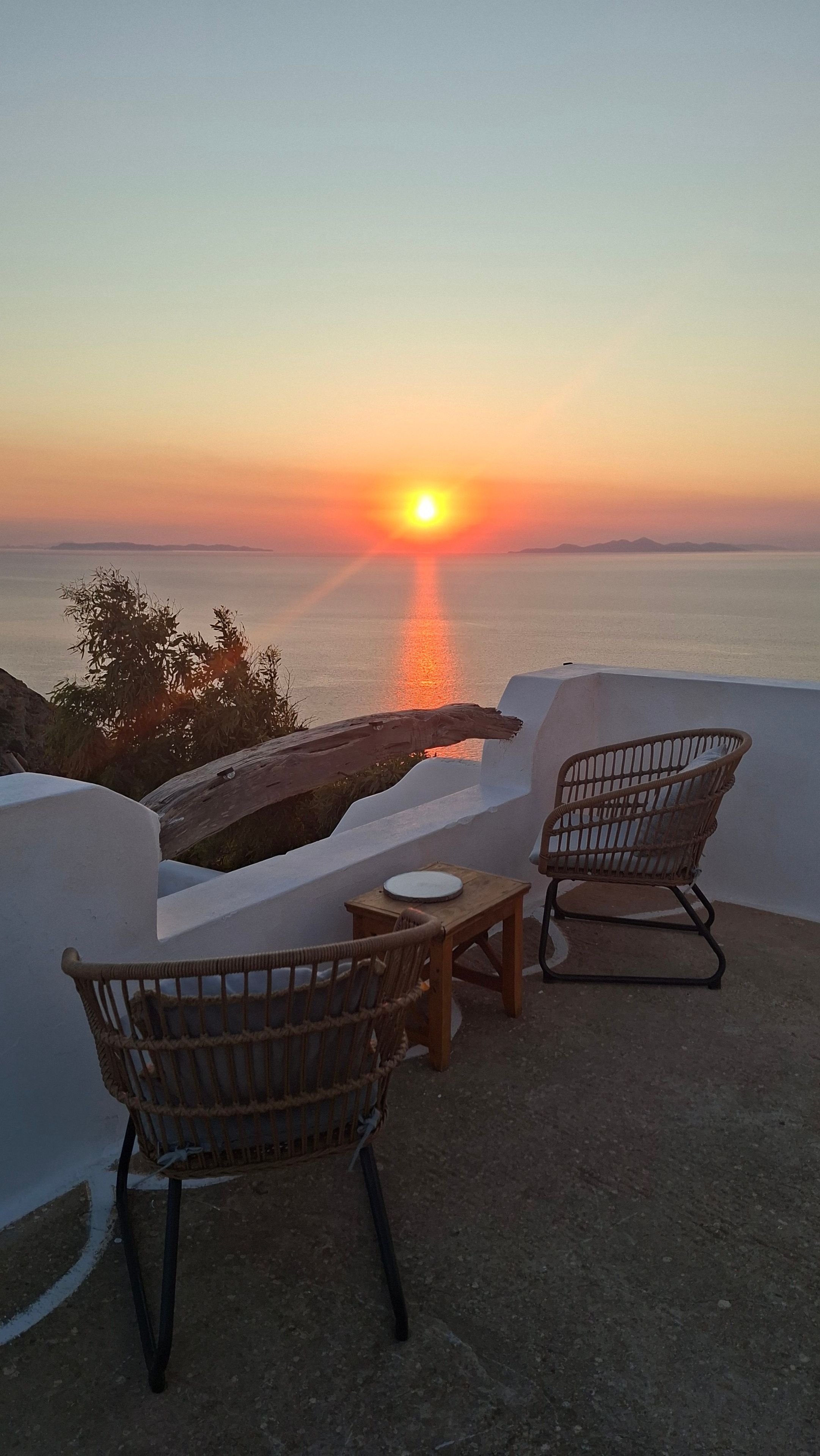 A sunset view from a balcony with two wicker chairs and a small table.