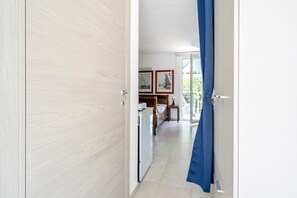 A hallway leading to a bedroom with a bed, a desk, and a window.