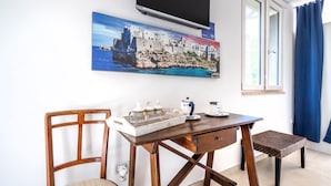 A room with a wooden desk, a chair, a small table, and a painting of a coastal town. - Villa Massa Depandance Apartment with Sea View, Wi-Fi and Air Conditioning (Polignano a Mare)