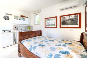 Ein Schlafzimmer mit einem Holzbett, einer kleinen Küchenzeile, einer Wanduhr und zwei gerahmten Bildern.