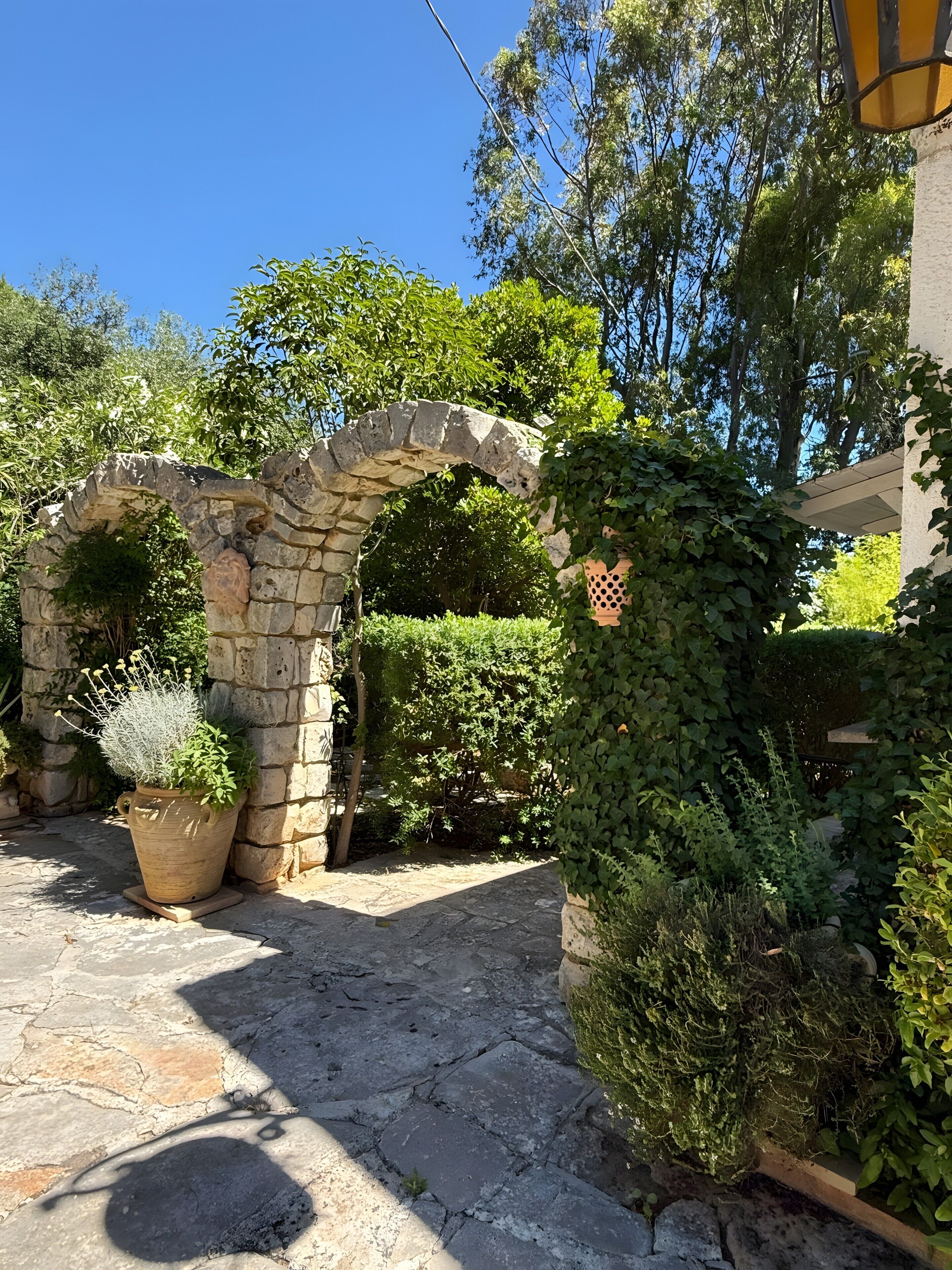 Ein steinernes Tor führt in einen Garten mit einem Blumentopf und einer Holzbank.