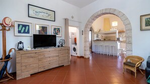 A modern living room with a wooden entertainment unit, a washing machine, and a kitchen area visible through an archway. - Apartment 'Villa Massa' with Sea View, Wi-Fi and Air Conditioning (Polignano a Mare)