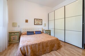 Een slaapkamer met een groot bed, een kledingkast, een nachtkastje en twee wandlampen.