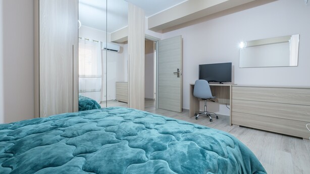 Ein Schlafzimmer mit einem Bett, einem Schreibtisch, einem Sessel und einem Fernseher.