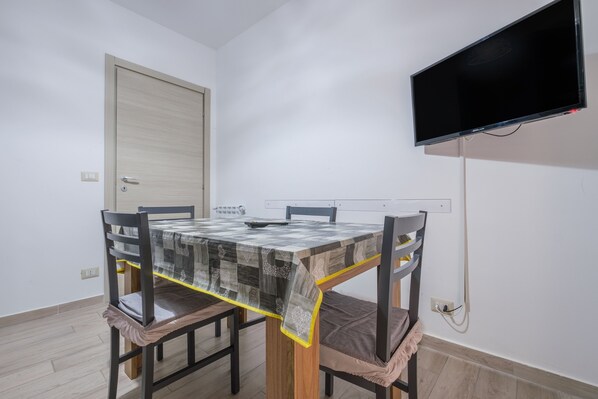 A dining area with a table, chairs, a TV mounted on the wall, and a door.