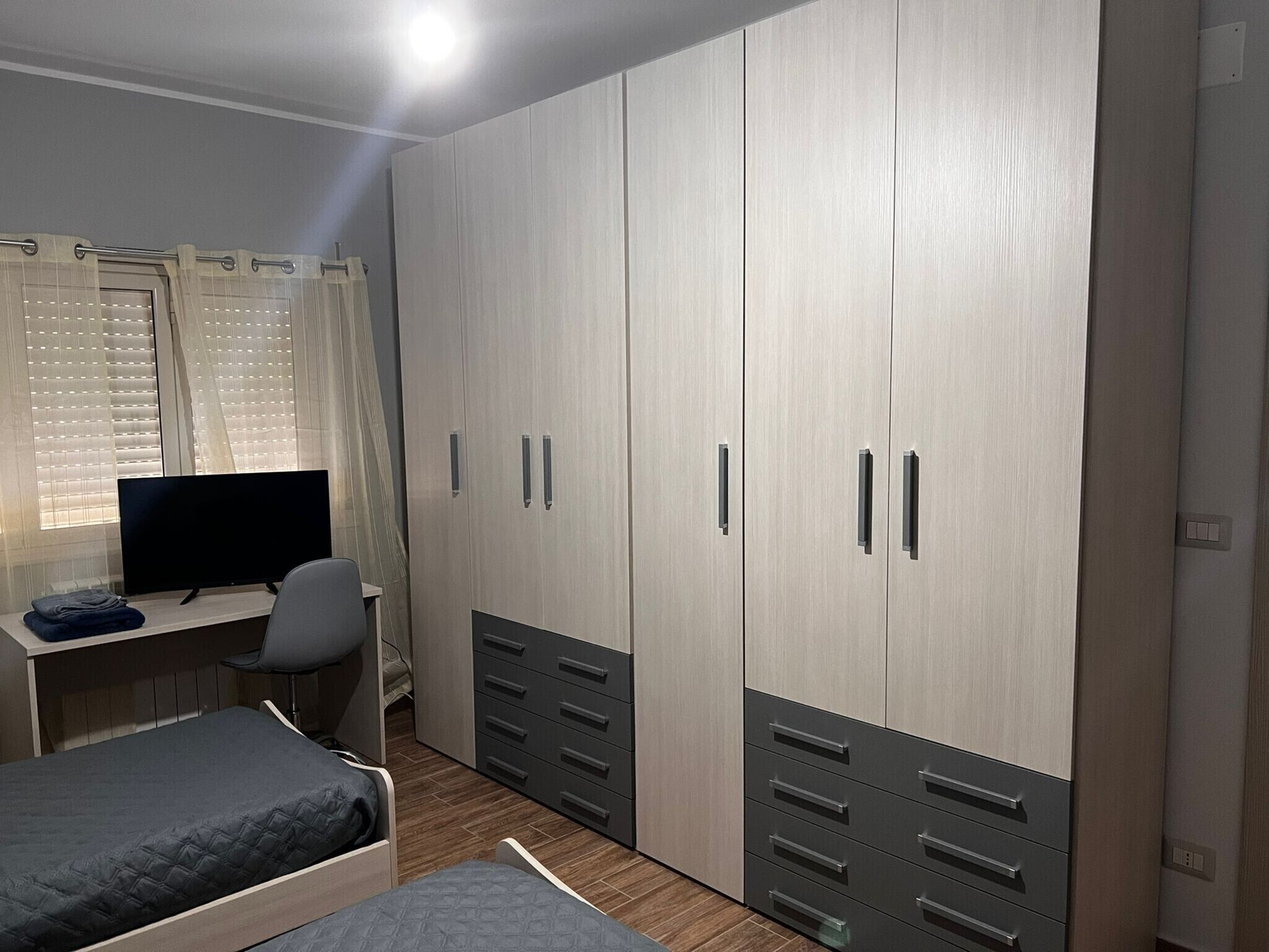 Una camera da letto con un letto, una scrivania, una televisione e un armadio con diversi cassetti e ante.