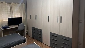 A bedroom with a bed, a desk, a TV, and a wardrobe with multiple drawers and doors.