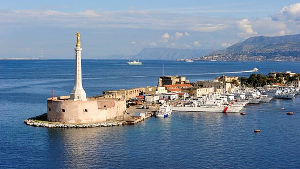 A coastal town with a prominent lighthouse, a marina with boats, and a historic fort.