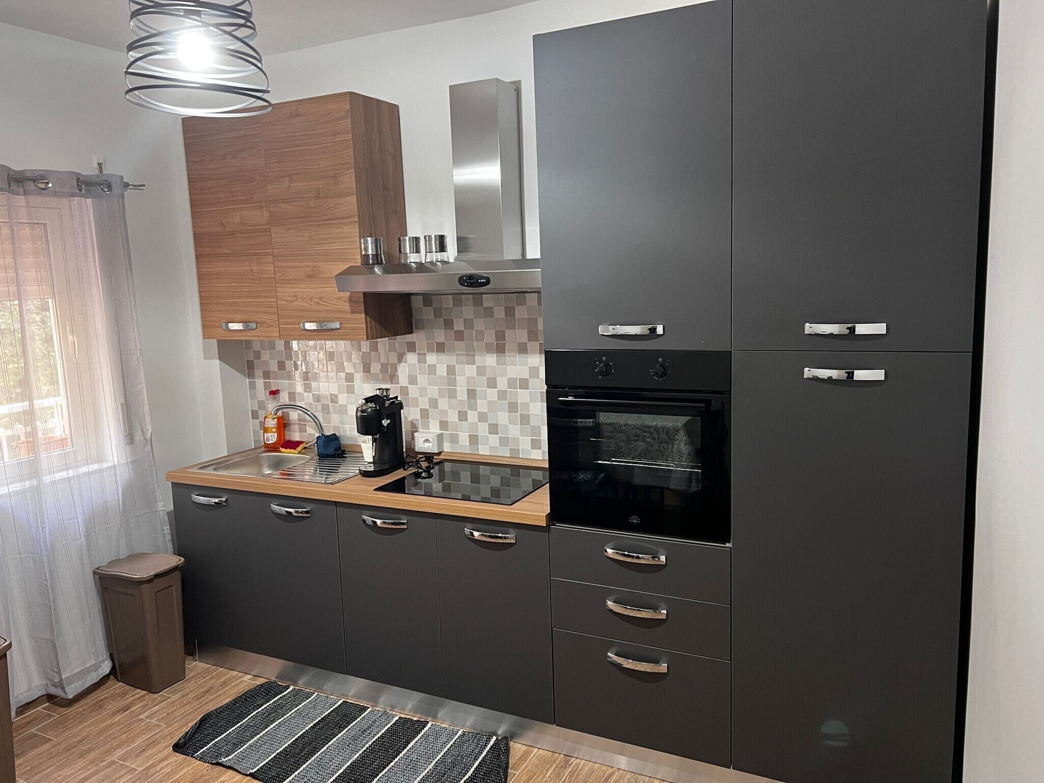 Una cucina moderna con mobili scuri, un forno integrato e una macchina da caffè sul piano di lavoro.