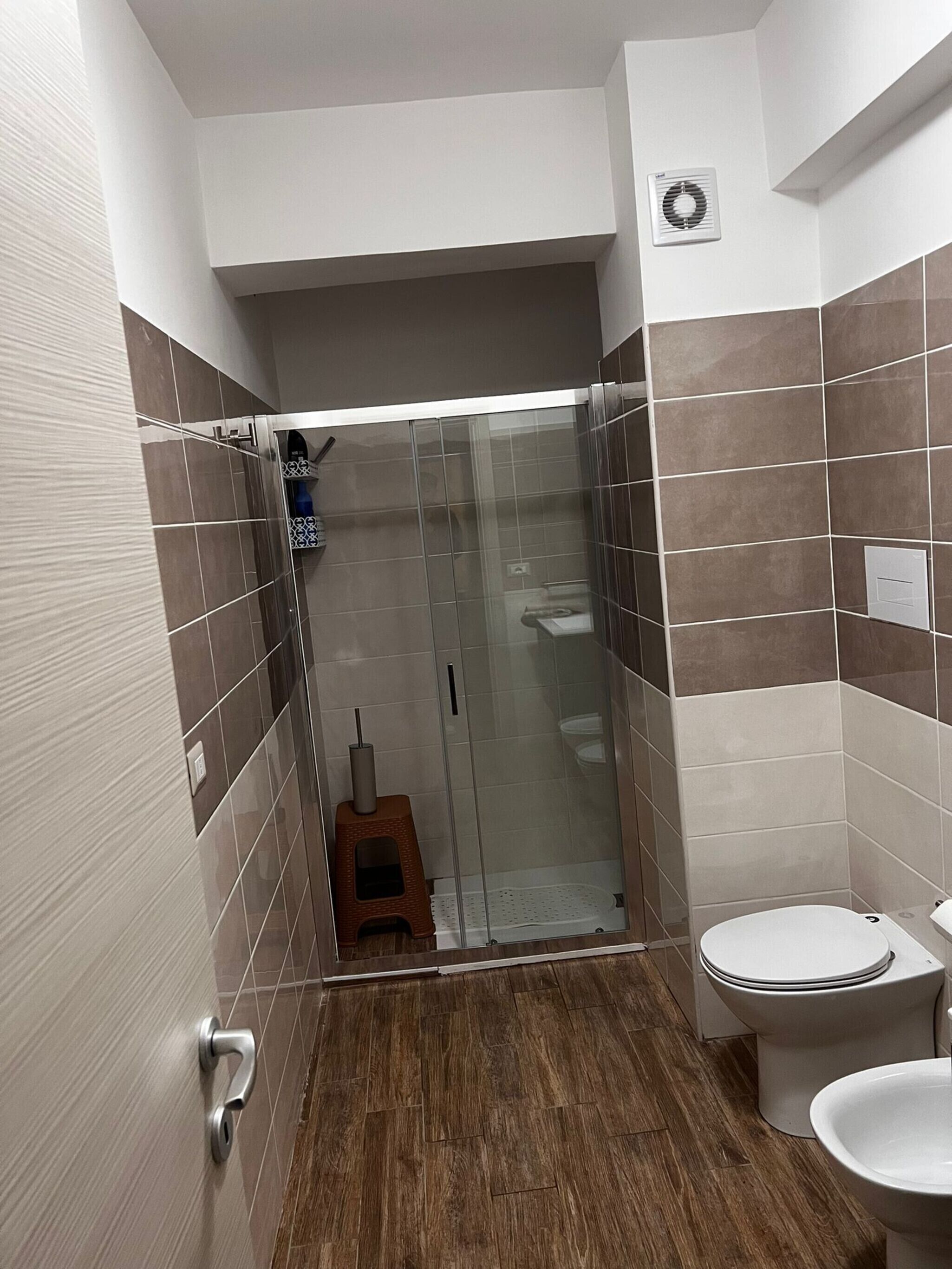Un bagno con doccia, WC e un piccolo sgabello.