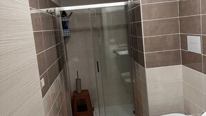 A bathroom with a shower, toilet, and a small stool.