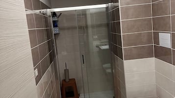 Un bagno con doccia, WC e un piccolo sgabello.