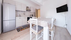 A modern kitchen with white cabinetry, a stainless steel refrigerator, and a dining area with a table and chairs.