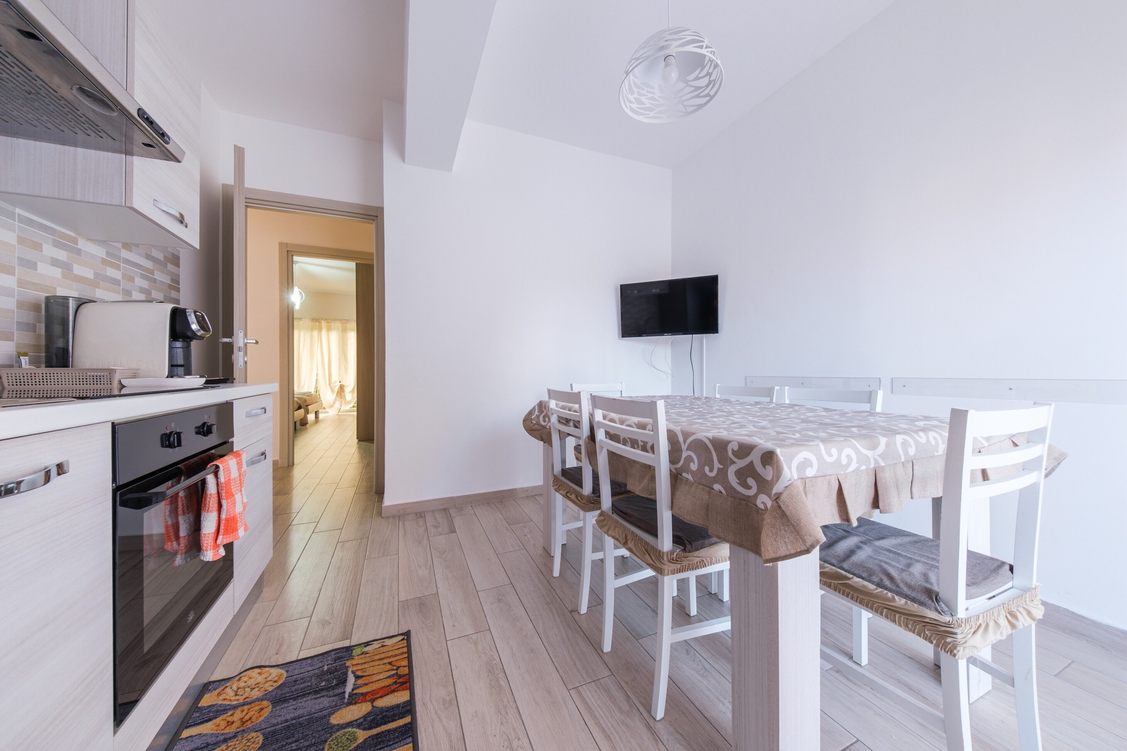 A modern kitchen with a built-in oven, a coffee machine, and a TV mounted on the wall.