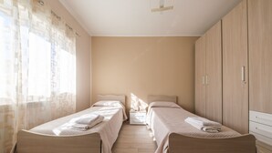 A bedroom with two beds, a wooden wardrobe, and a window with curtains.