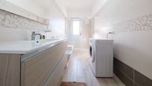 A modern bathroom with a sink, mirror, toilet, and washing machine.