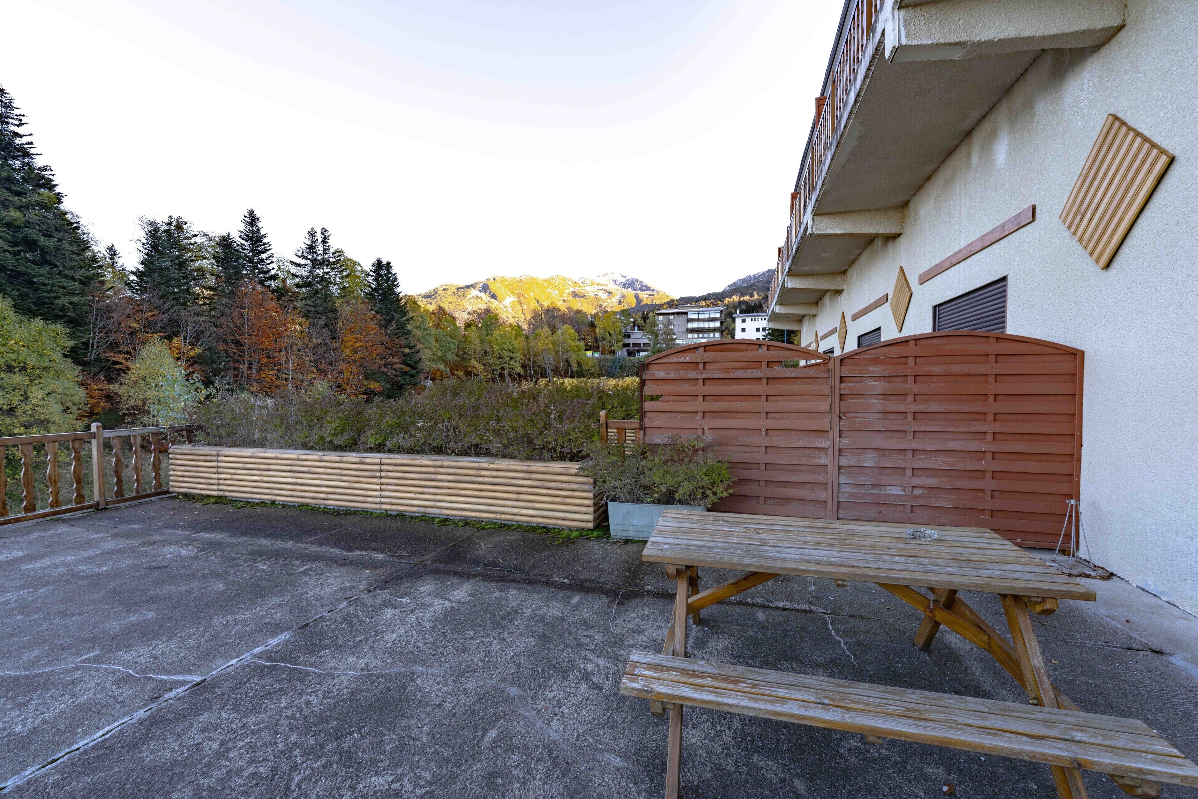 Une terrasse en béton avec une table et des bancs en bois, une clôture en bois et une vue sur une montagne.