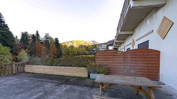 Une terrasse en béton avec une table et des bancs en bois, une clôture en bois et une vue sur une montagne.