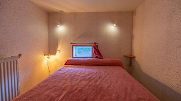 A bedroom with a bed, a window with curtains, a radiator, and wall-mounted lights.