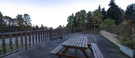 A picnic table on a concrete deck with a railing, surrounded by trees and a clear sky.