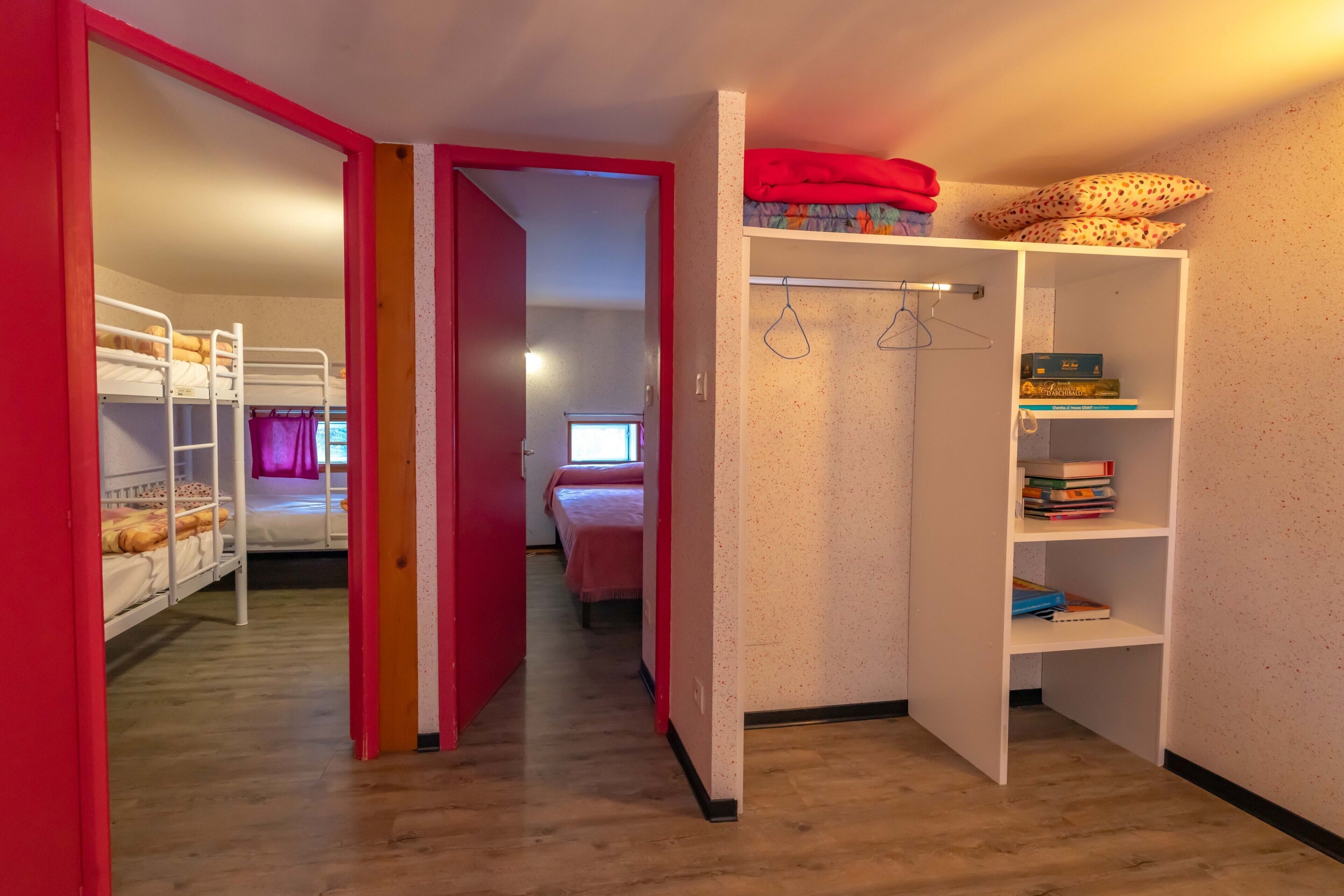 Una habitación con literas, un armario con espacio para colgar ropa y una estantería.