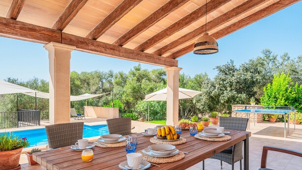 An outdoor dining area with a pool view, wooden pergola, and potted plants. - Villa 'Can Rito Nou' with Mountain View, Wi-Fi and Air Conditioning (Felanitx)
